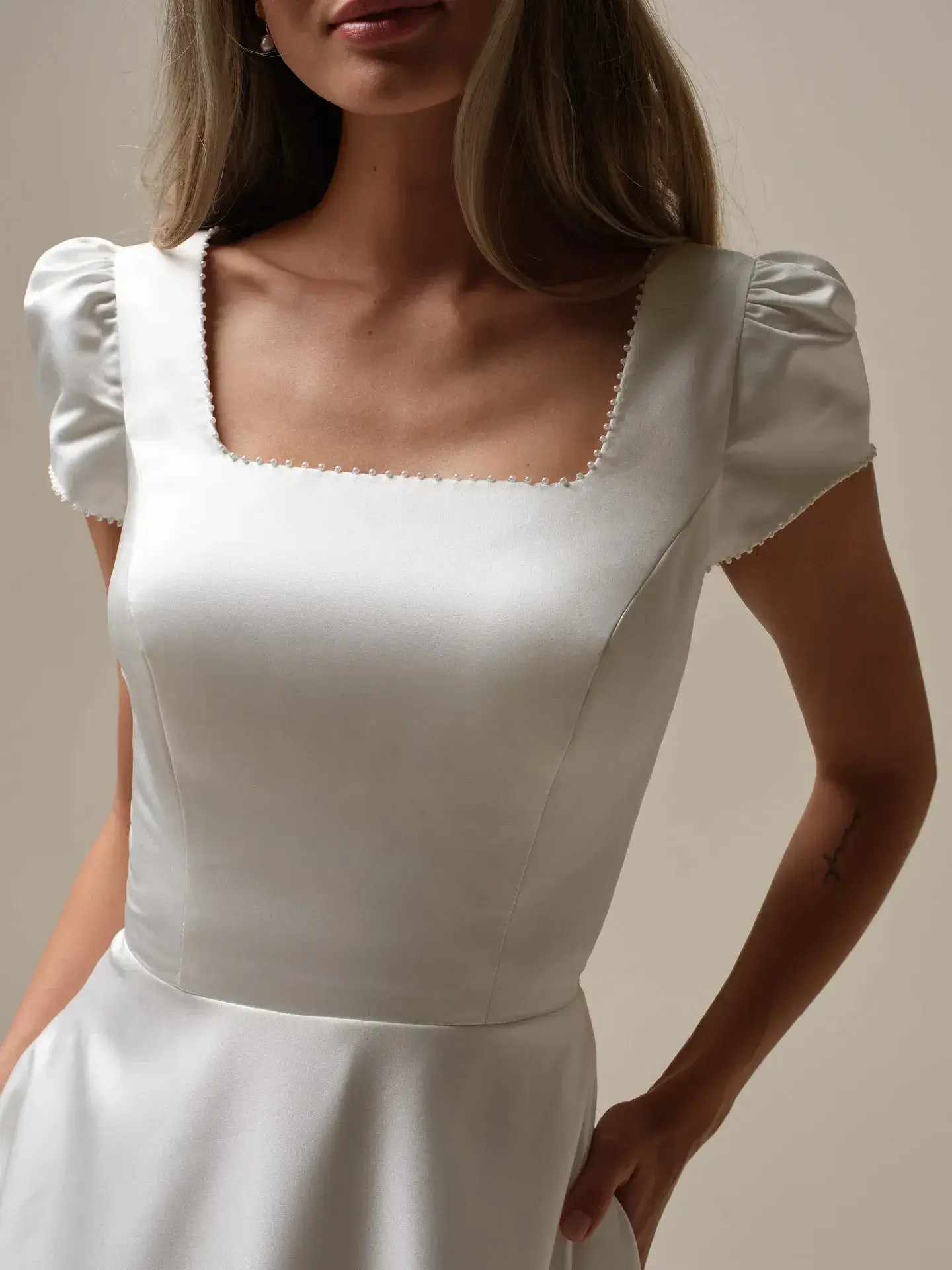 Model is wearing a satin wedding dress with puff sleeves by rebecca ingram