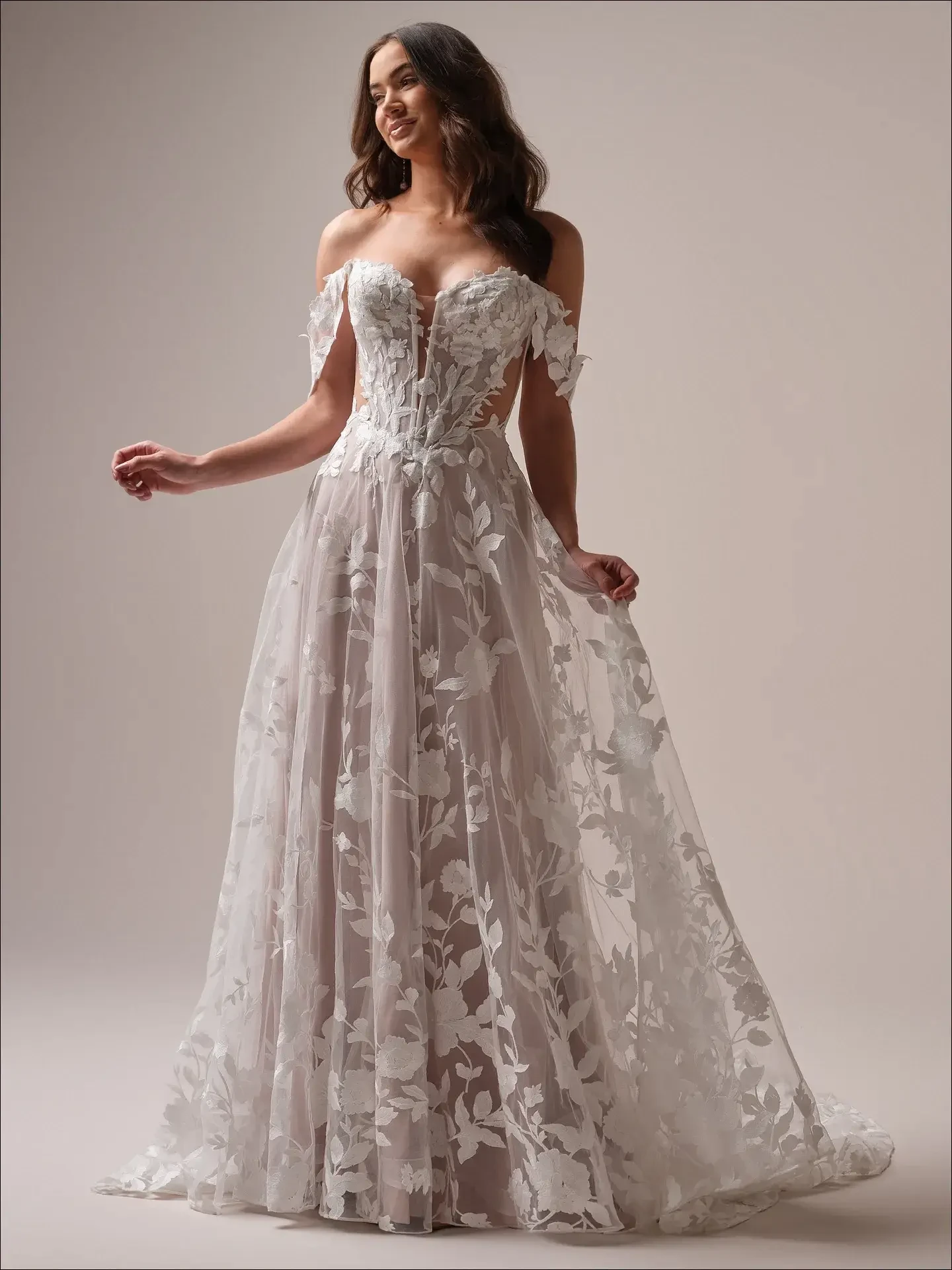 Model is wearing a floral-inspired A-line wedding gown with illusion panels and an off-the-shoulder neckline.