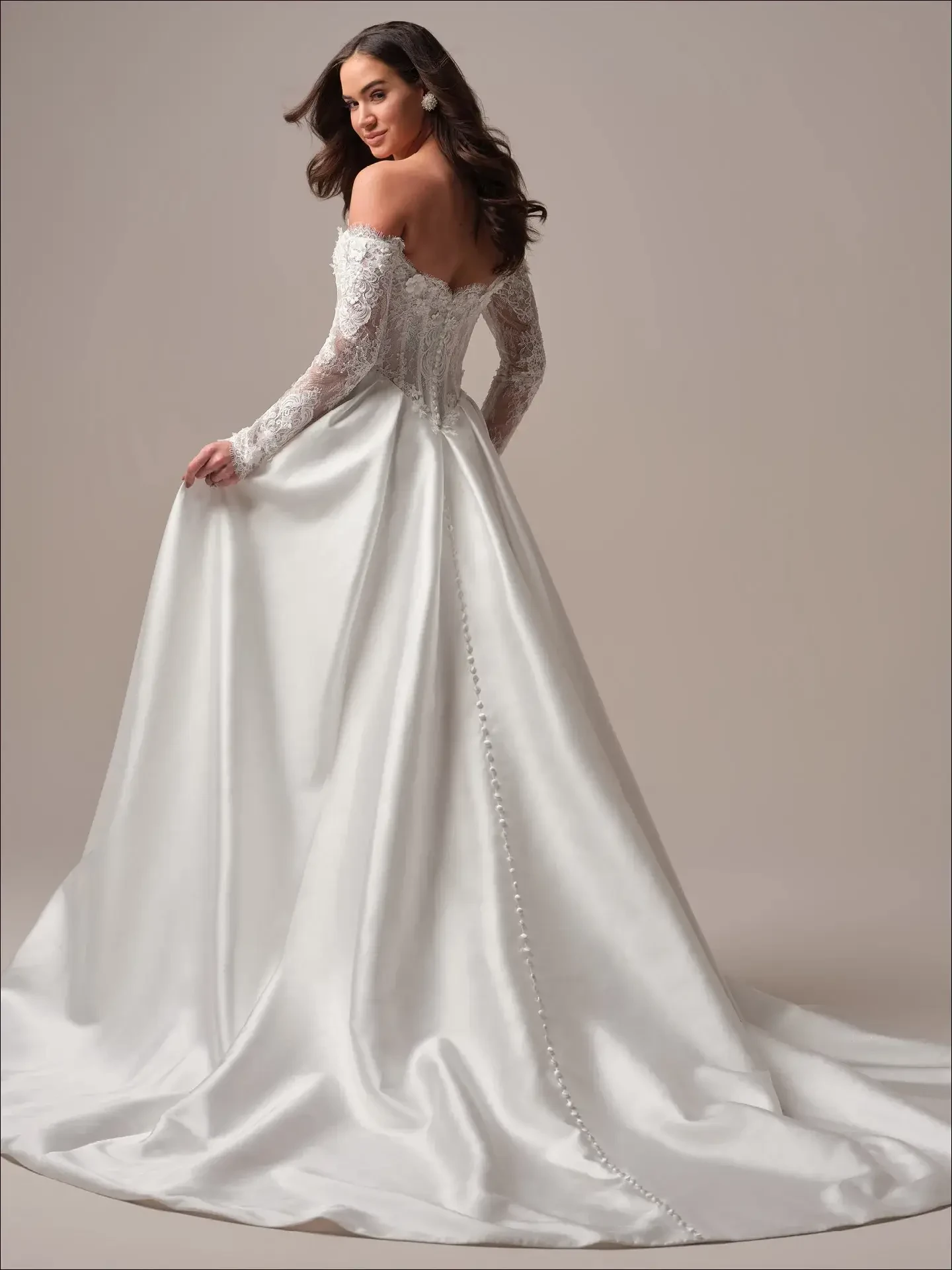 Model is wearing an off-the-shoulder lace A-line wedding gown with long sleeves, a high slit, and a sophisticated silhouette.