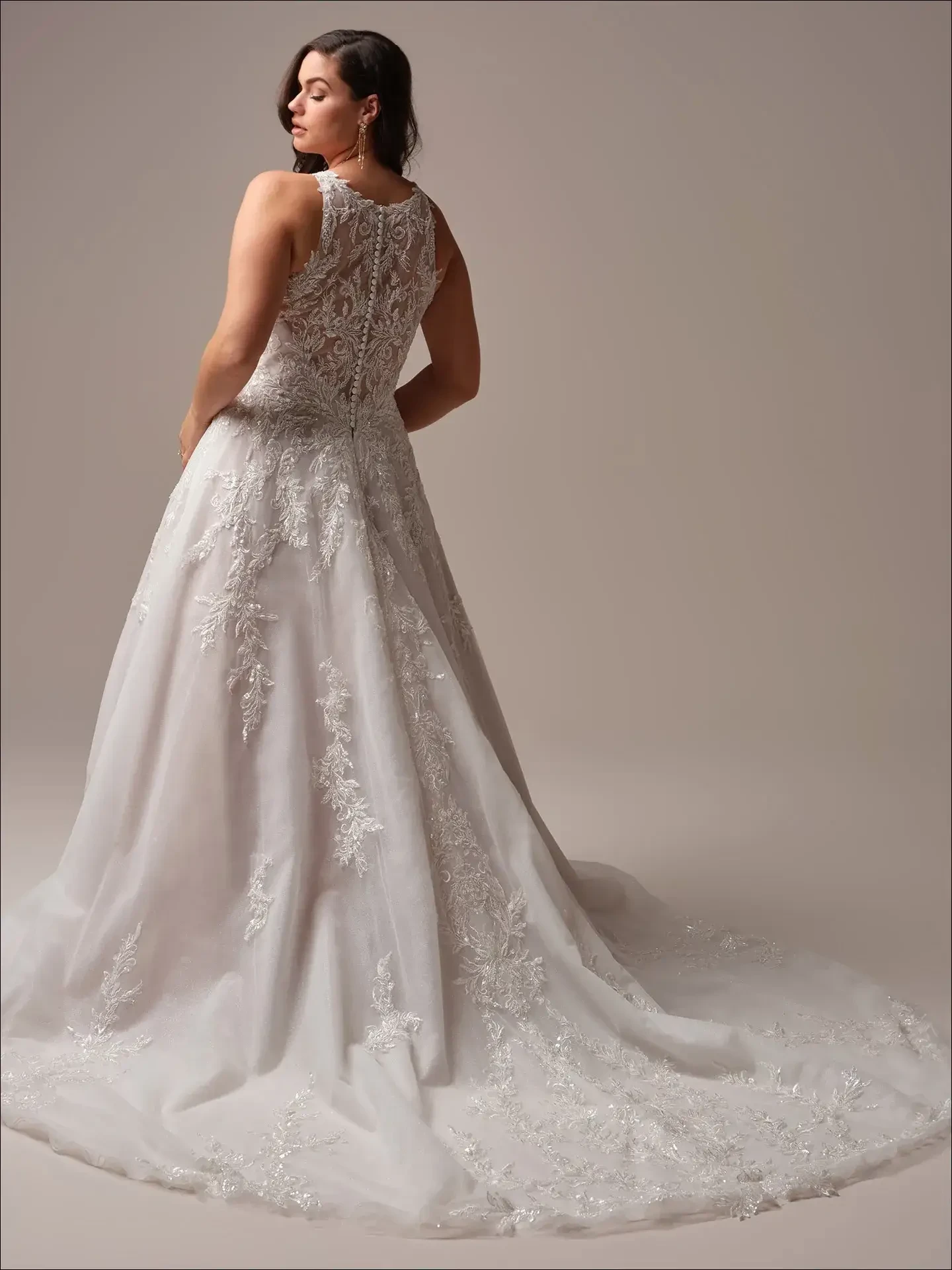 Model is wearing a halter-neck A-line wedding gown with shimmering tulle, beaded lace, an illusion back, and pockets.